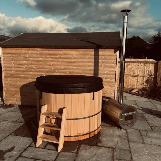 photograph of a wooden hot tub with a wood burner next to it