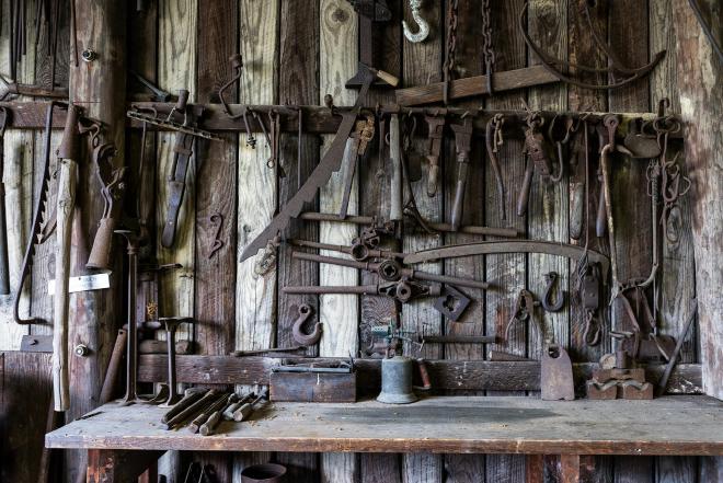 Metal, slightly rusted tools hanging above a wooden workbench.
